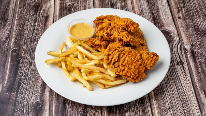 A white plate holds crispy fried chicken tenders, golden french fries, and a cup of dipping sauce.