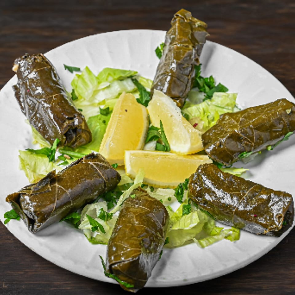Dolmades appetizer with fresh lemon wedges and lettuce on a white plate.