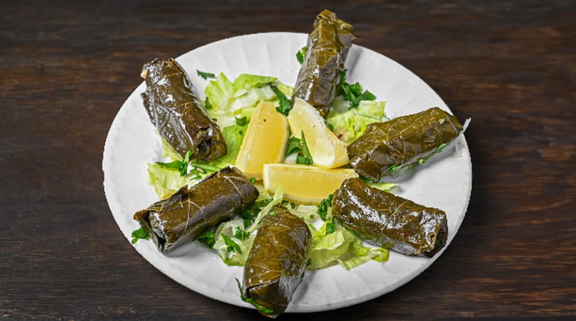 Dolmades appetizer with fresh lemon wedges and lettuce on a white plate.