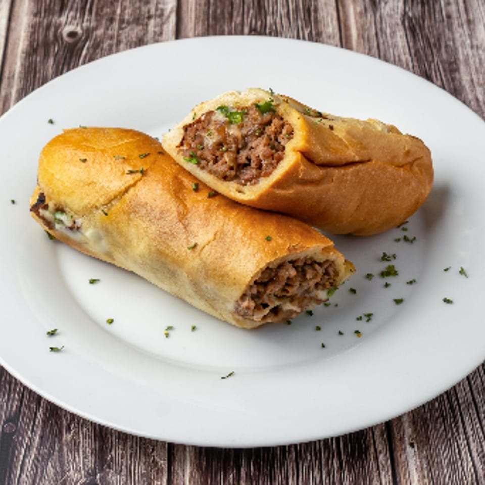 Two halves of a meat and cheese sub sandwich on a white plate, garnished with herbs.