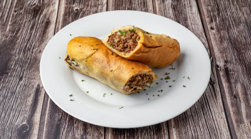 Two halves of a meat and cheese sub sandwich on a white plate, garnished with herbs.