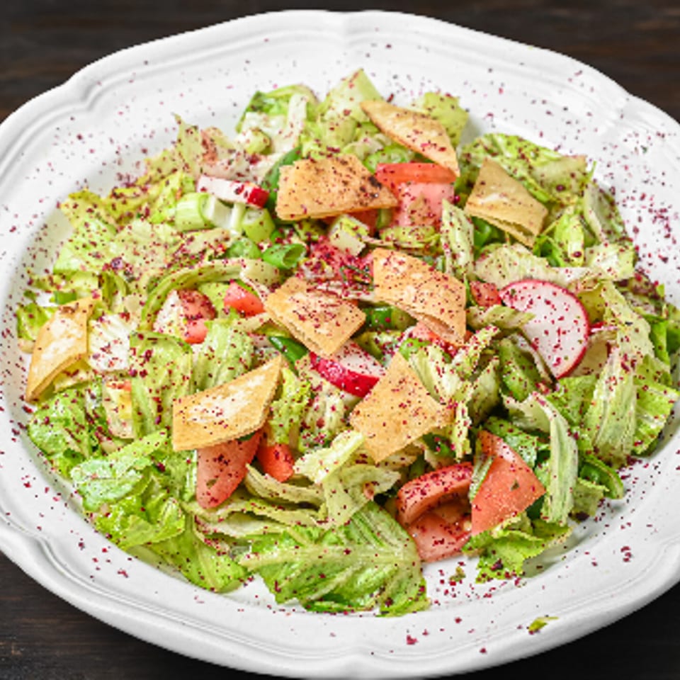 Fattoush salad with crisp lettuce, tomatoes, radishes, pita chips, and sumac on a white plate.
