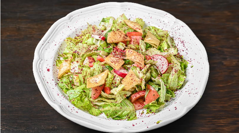 Fattoush salad with crisp lettuce, tomatoes, radishes, pita chips, and sumac on a white plate.